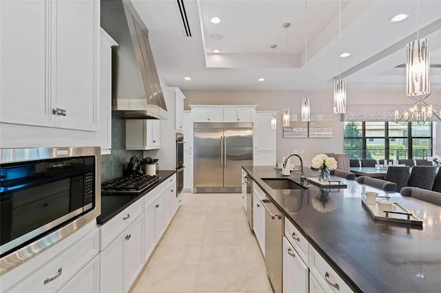 kitchen featuring white cabinets, built in appliances, pendant lighting, a tray ceiling, and sink