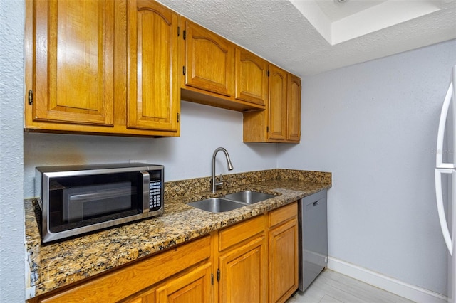 kitchen featuring sink, fridge, a textured ceiling, dishwasher, and dark stone counters