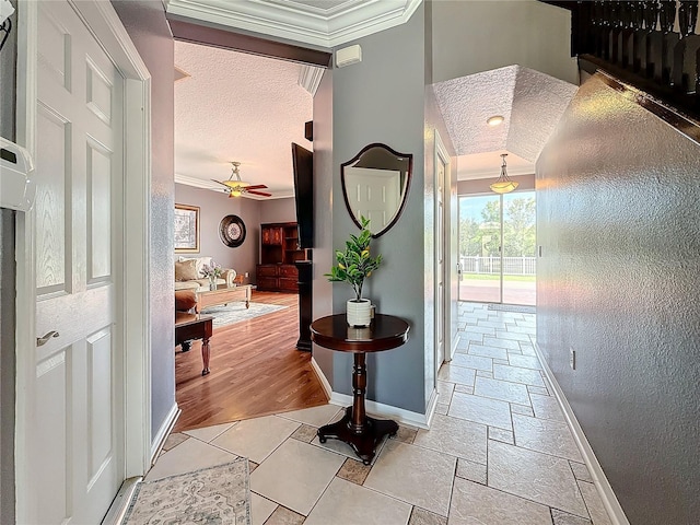 corridor with a textured ceiling, a textured wall, stone tile floors, baseboards, and crown molding