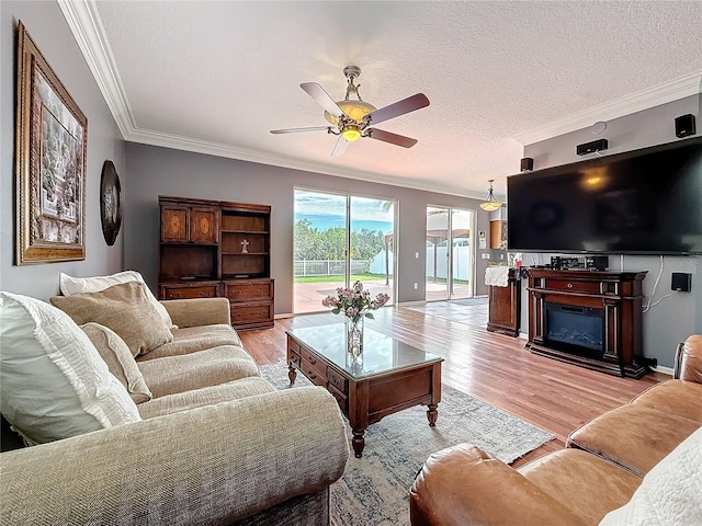 living room with a textured ceiling, a ceiling fan, ornamental molding, light wood finished floors, and a glass covered fireplace