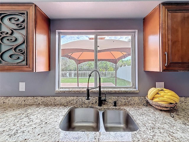 kitchen with light stone countertops, a wealth of natural light, brown cabinetry, and a sink