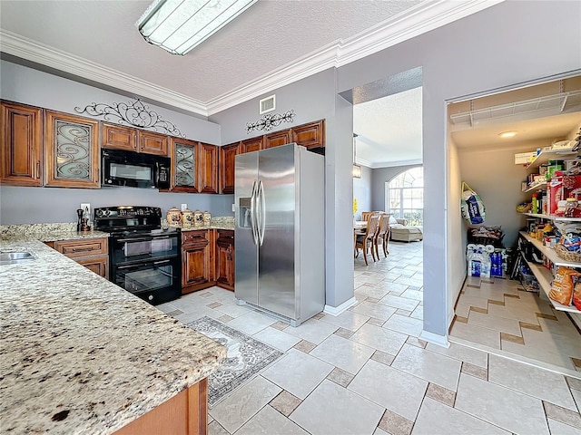 kitchen featuring a textured ceiling, light stone counters, black appliances, brown cabinetry, and crown molding