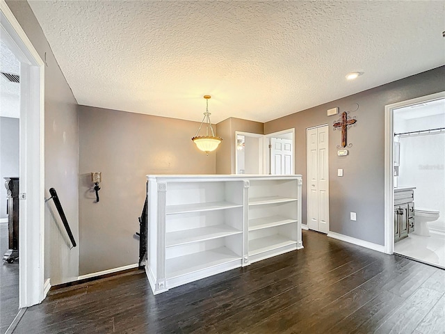 unfurnished dining area featuring dark wood-style flooring, a textured ceiling, and baseboards