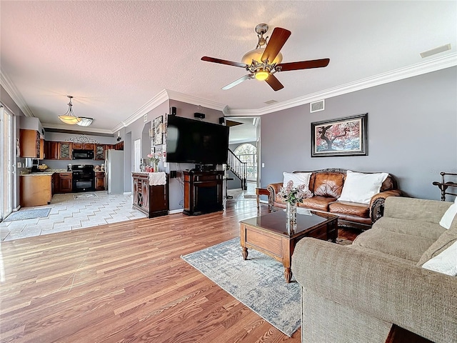 living area featuring light wood-style floors, ornamental molding, ceiling fan, and visible vents