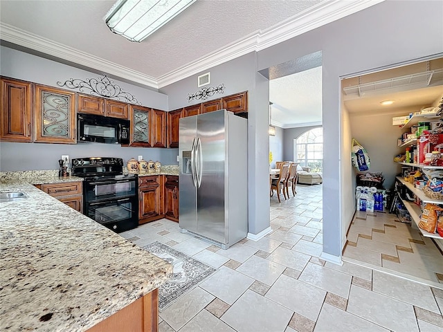 kitchen featuring brown cabinetry, ornamental molding, a textured ceiling, light stone counters, and black appliances