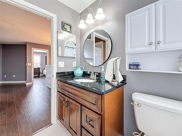 bathroom with vanity, wood finished floors, toilet, baseboards, and a textured ceiling