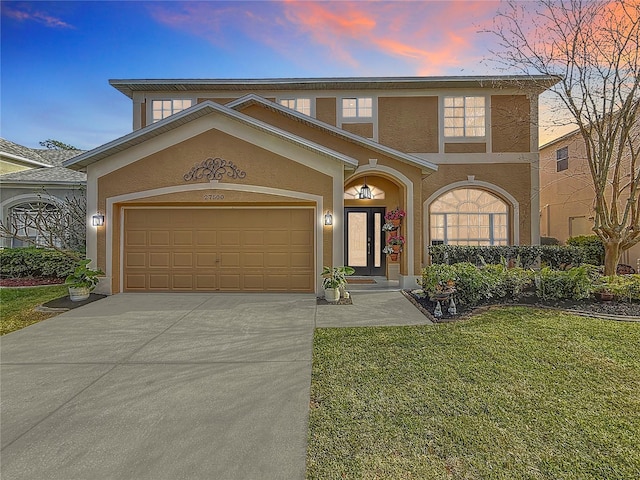 mediterranean / spanish house with a lawn, an attached garage, driveway, and stucco siding