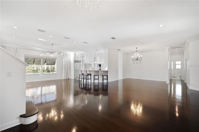 unfurnished living room featuring dark hardwood / wood-style flooring, ornamental molding, and an inviting chandelier