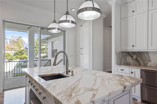 kitchen featuring decorative light fixtures, a kitchen island with sink, light stone countertops, white cabinets, and sink