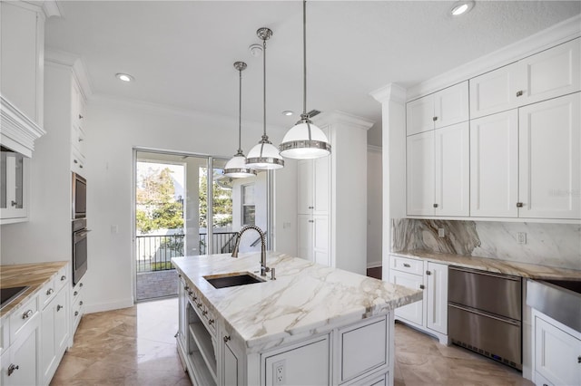 kitchen with decorative light fixtures, white cabinetry, an island with sink, decorative backsplash, and sink