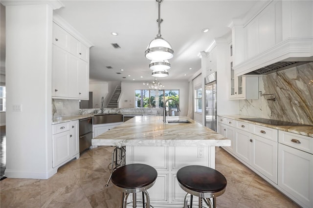 kitchen featuring a breakfast bar, sink, hanging light fixtures, an island with sink, and stainless steel built in refrigerator