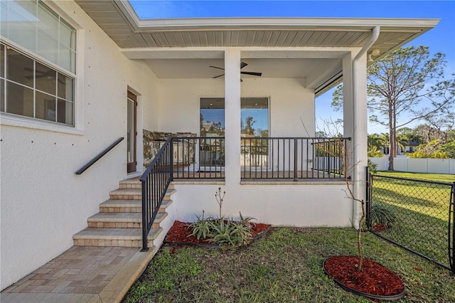 view of exterior entry with ceiling fan and a lawn