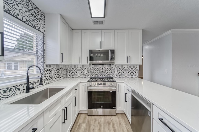 kitchen with appliances with stainless steel finishes, white cabinetry, crown molding, and sink