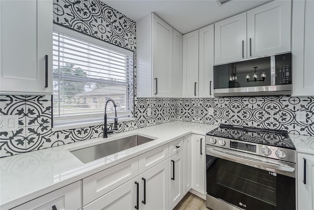 kitchen featuring appliances with stainless steel finishes, light stone counters, sink, white cabinetry, and backsplash