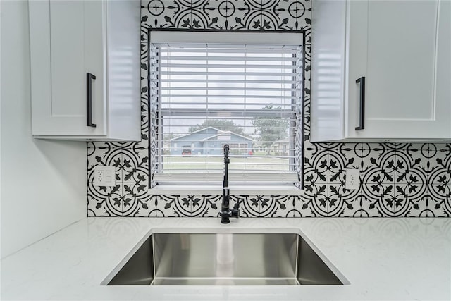 room details with light stone counters, white cabinetry, decorative backsplash, and sink