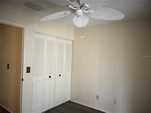 unfurnished bedroom featuring a textured ceiling, ceiling fan, a closet, and dark hardwood / wood-style floors