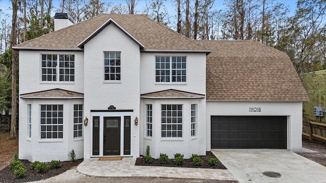 traditional-style house with a shingled roof, concrete driveway, a chimney, an attached garage, and brick siding