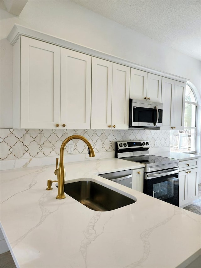 kitchen featuring light stone countertops, sink, stainless steel appliances, and white cabinetry