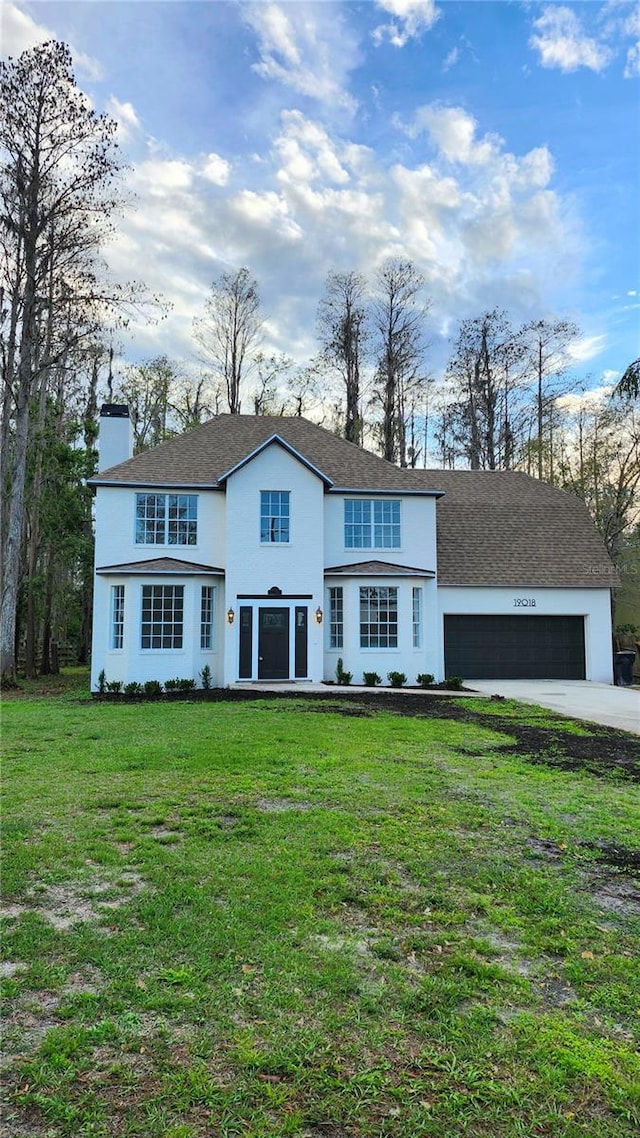 traditional-style house featuring driveway, a front lawn, a chimney, and an attached garage