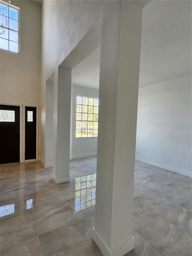 entrance foyer with marble finish floor, a towering ceiling, and baseboards