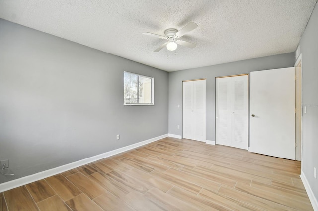 unfurnished bedroom with a textured ceiling, ceiling fan, and multiple closets