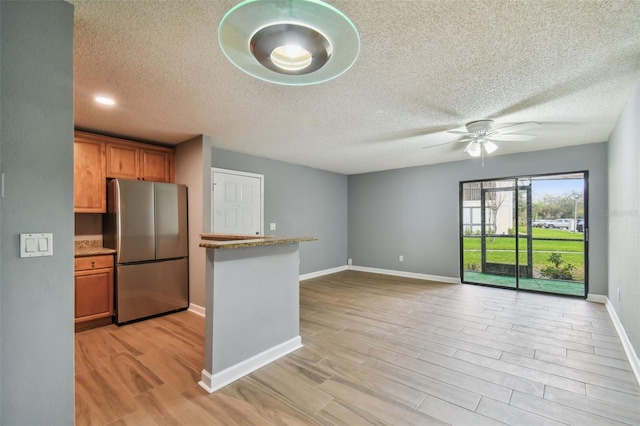 kitchen featuring light hardwood / wood-style floors, stainless steel refrigerator, ceiling fan, and light stone counters