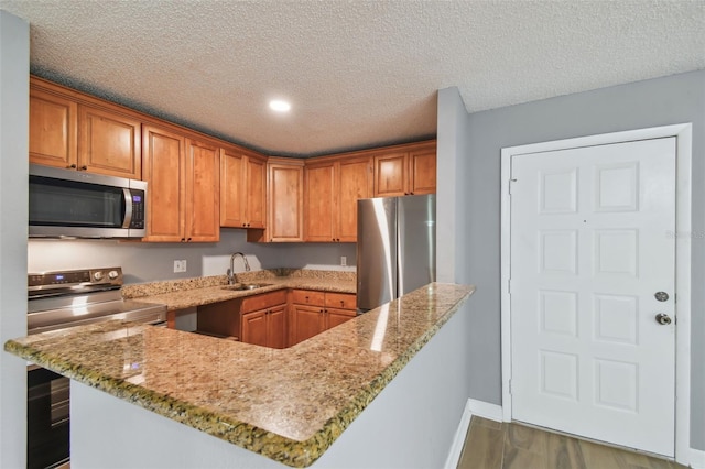 kitchen with stainless steel appliances, sink, a textured ceiling, kitchen peninsula, and light stone countertops