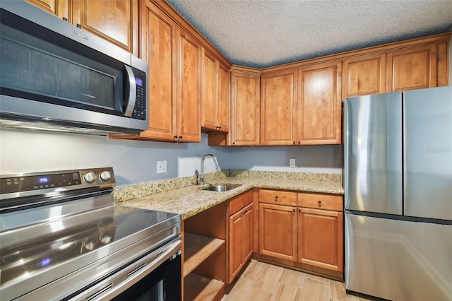 kitchen featuring appliances with stainless steel finishes, light stone countertops, sink, and a textured ceiling