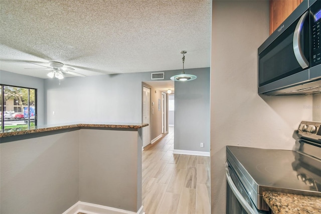 kitchen featuring dark stone countertops, appliances with stainless steel finishes, ceiling fan, a textured ceiling, and decorative light fixtures