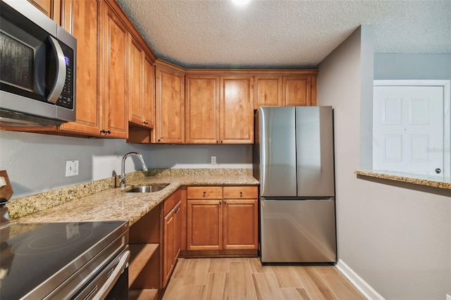 kitchen featuring sink, a textured ceiling, light stone counters, light wood-type flooring, and appliances with stainless steel finishes