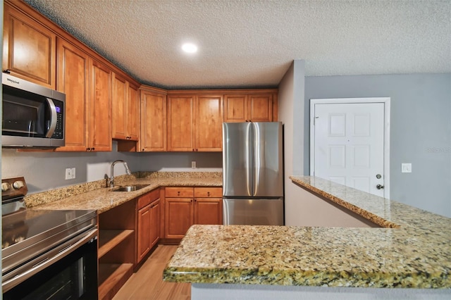 kitchen featuring light stone counters, a textured ceiling, stainless steel appliances, light wood-type flooring, and sink