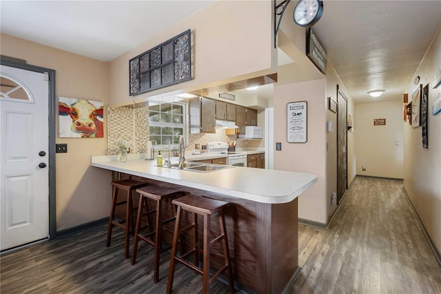 kitchen featuring dark hardwood / wood-style floors, a kitchen breakfast bar, kitchen peninsula, white appliances, and decorative backsplash