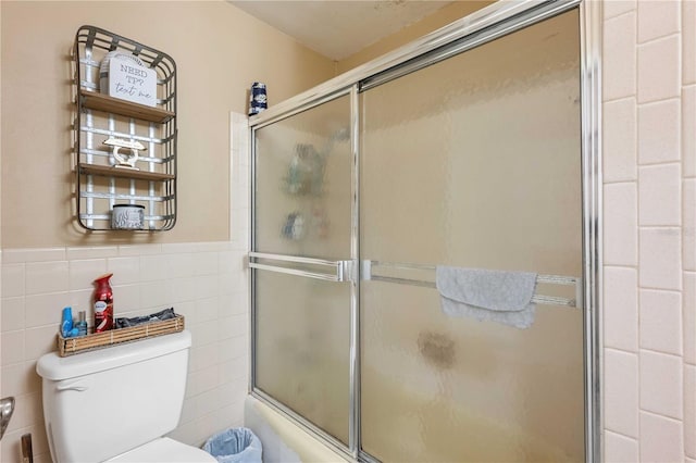 bathroom featuring enclosed tub / shower combo, wainscoting, toilet, and tile walls