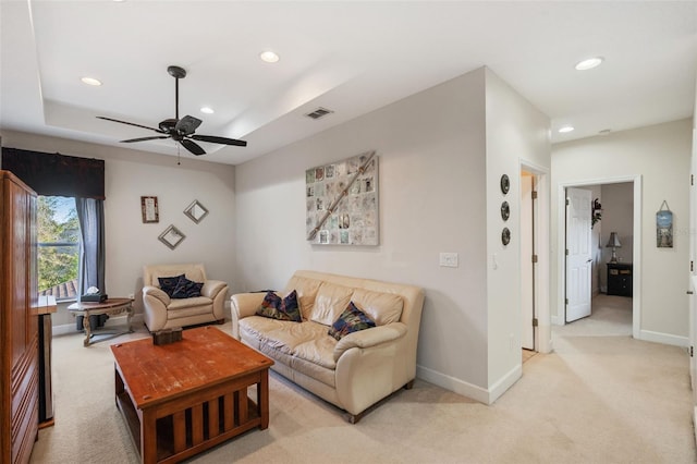 carpeted living room with ceiling fan and a tray ceiling