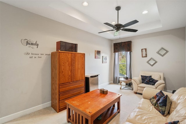 living room with light colored carpet, a raised ceiling, and ceiling fan