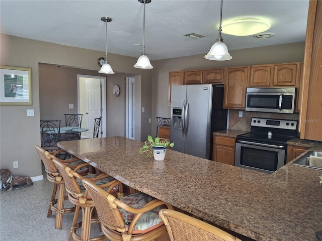 kitchen with sink, hanging light fixtures, stainless steel appliances, tasteful backsplash, and a kitchen bar