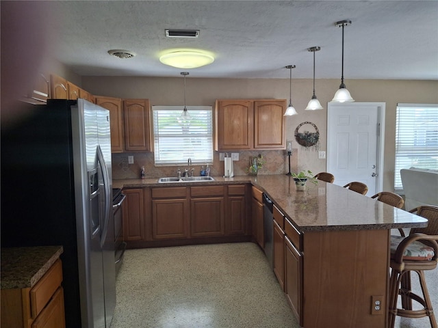 kitchen with sink, dark stone countertops, appliances with stainless steel finishes, a kitchen breakfast bar, and pendant lighting