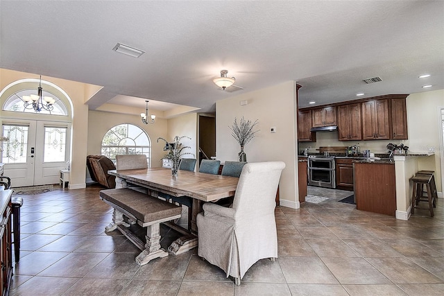 dining space featuring a tray ceiling, an inviting chandelier, a textured ceiling, light tile patterned floors, and french doors