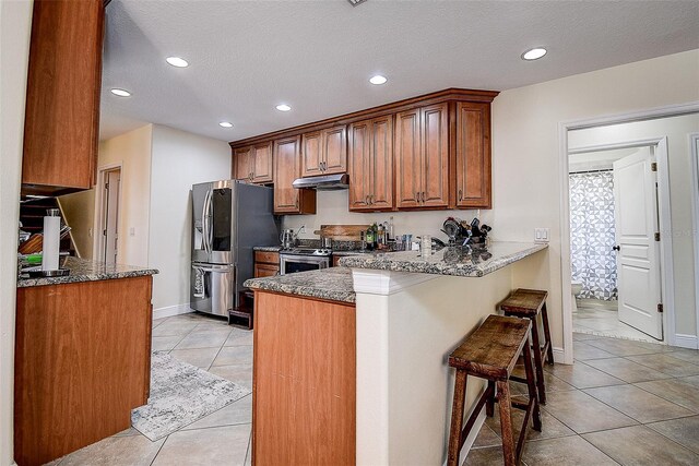 kitchen with a breakfast bar, appliances with stainless steel finishes, kitchen peninsula, and dark stone counters