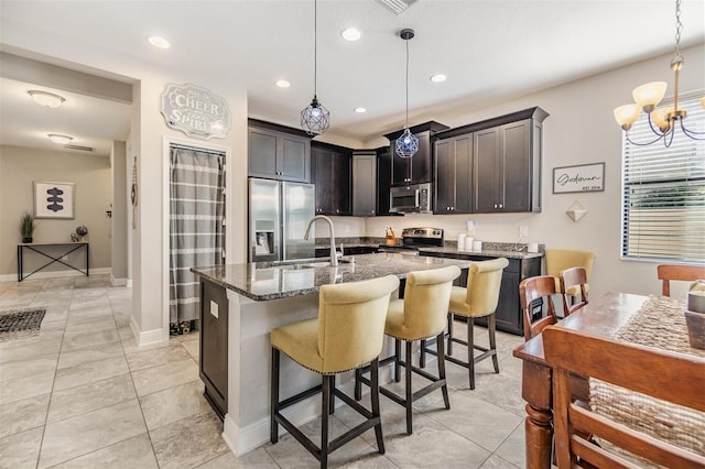 kitchen featuring a kitchen island with sink, stainless steel appliances, pendant lighting, dark brown cabinetry, and sink