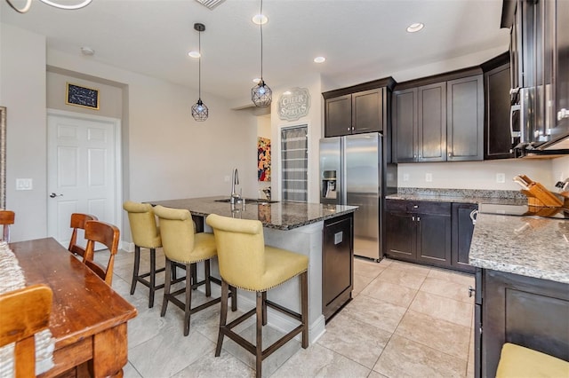 kitchen featuring sink, decorative light fixtures, an island with sink, dark stone counters, and stainless steel fridge with ice dispenser