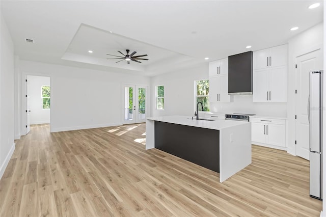 kitchen featuring a center island with sink, a tray ceiling, refrigerator, white cabinets, and sink