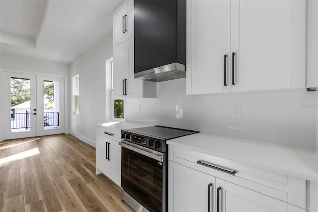 kitchen featuring french doors, wall chimney exhaust hood, stainless steel electric stove, and white cabinetry