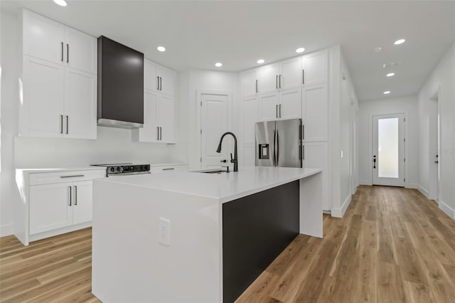 kitchen featuring white cabinets, stainless steel fridge, an island with sink, and light hardwood / wood-style floors