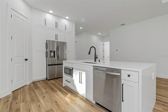 kitchen with sink, white cabinets, stainless steel appliances, and a kitchen island with sink