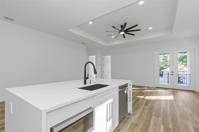 kitchen featuring white cabinetry, stainless steel appliances, an island with sink, sink, and a raised ceiling