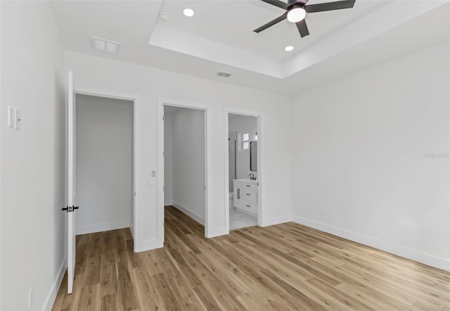 unfurnished bedroom featuring ceiling fan, connected bathroom, light hardwood / wood-style flooring, and a tray ceiling