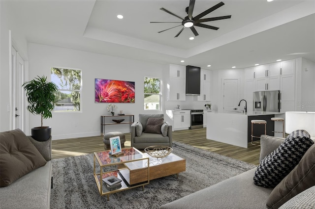 living area featuring baseboards, light wood-type flooring, a raised ceiling, and recessed lighting