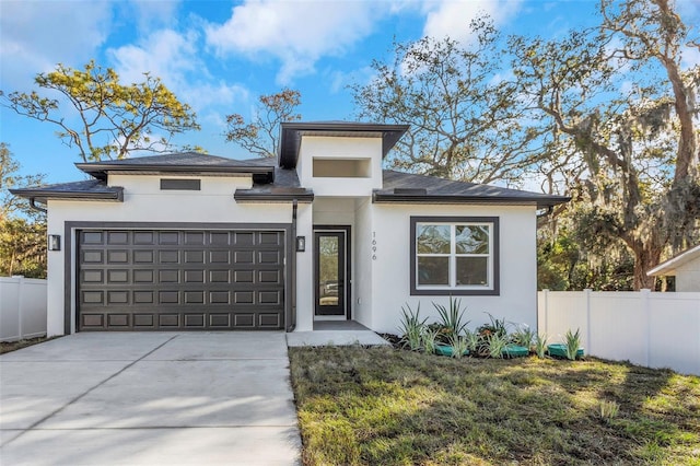 prairie-style house with a garage, concrete driveway, fence, and stucco siding