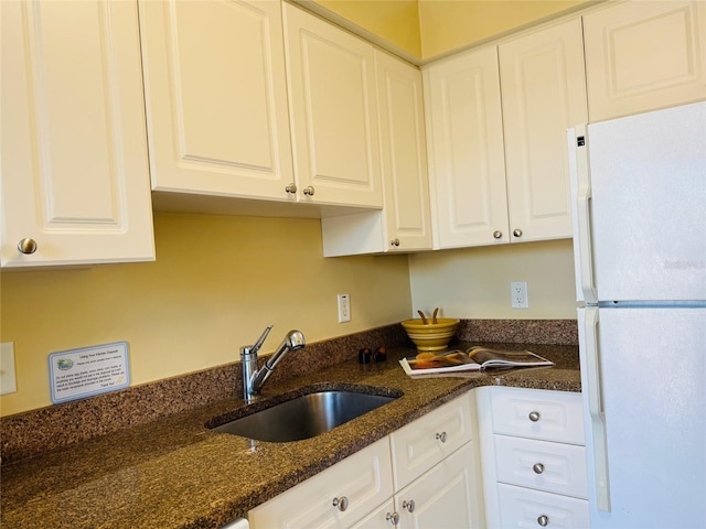 kitchen with dark stone countertops, white cabinets, a sink, and freestanding refrigerator